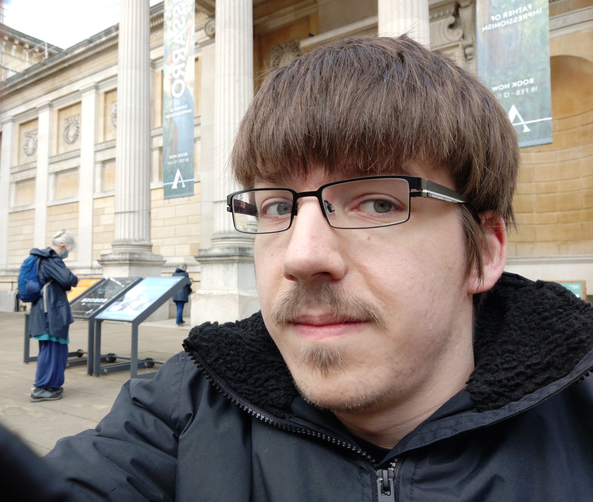 Kyle is a young man in glasses with moustache in front of doric columns of Ashmolean Museum.