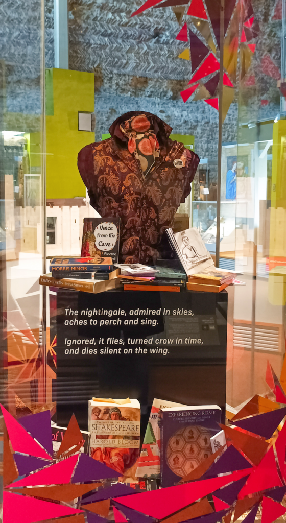 Karl's Un/Masked display, which features a bust wearing a paisley jacket and a decorative scarf, and a selection of books.