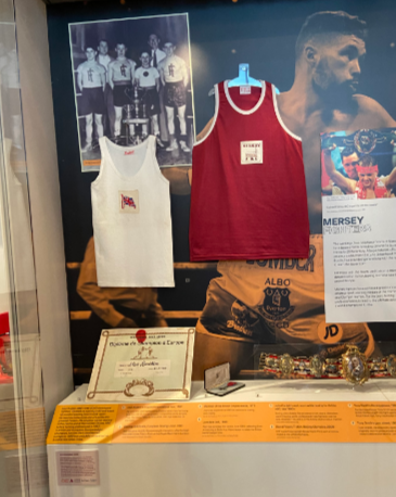 Alan Rudkin’s vests, a boxing certificate, his MBE medal, and a championship belt in the Wondrous Place gallery, Museum of Liverpool, with the new labels Iris created